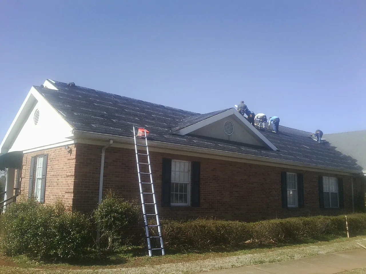 Crew tearing shingles off a brick ranch roof with a ladder set — Emergency Roof Repair work by our crew in Tarboro