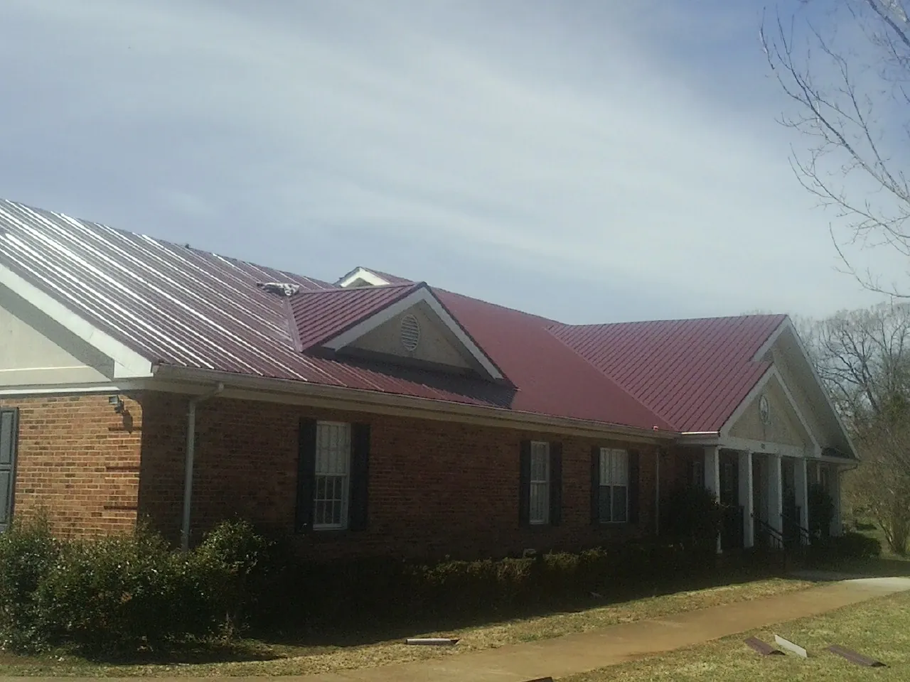 Red metal roof with gabled entries on a long brick building, from a Hail Damage Roof Repair job in Tarboro