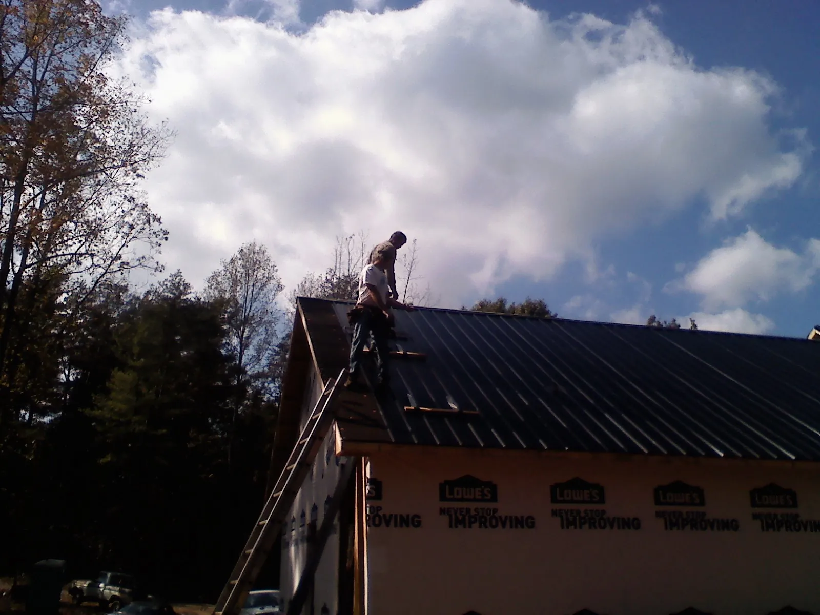 Roofer fastening dark metal panels high against a cloudy sky, from a Roof Inspection job in Tarboro