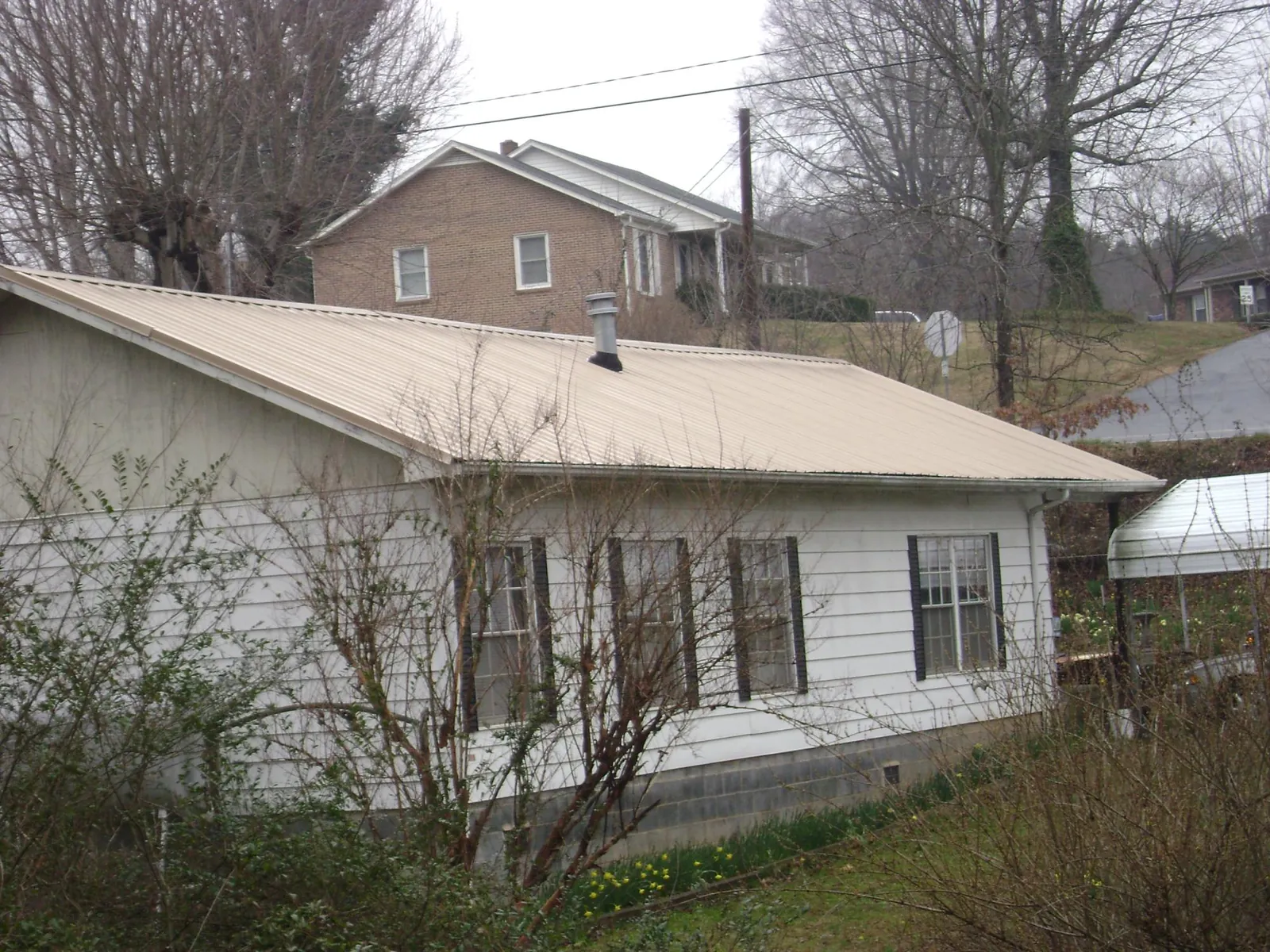Tan metal roof on a white sided house set into a hillside — Commercial Roofing by Roofing Brothers in Tarboro