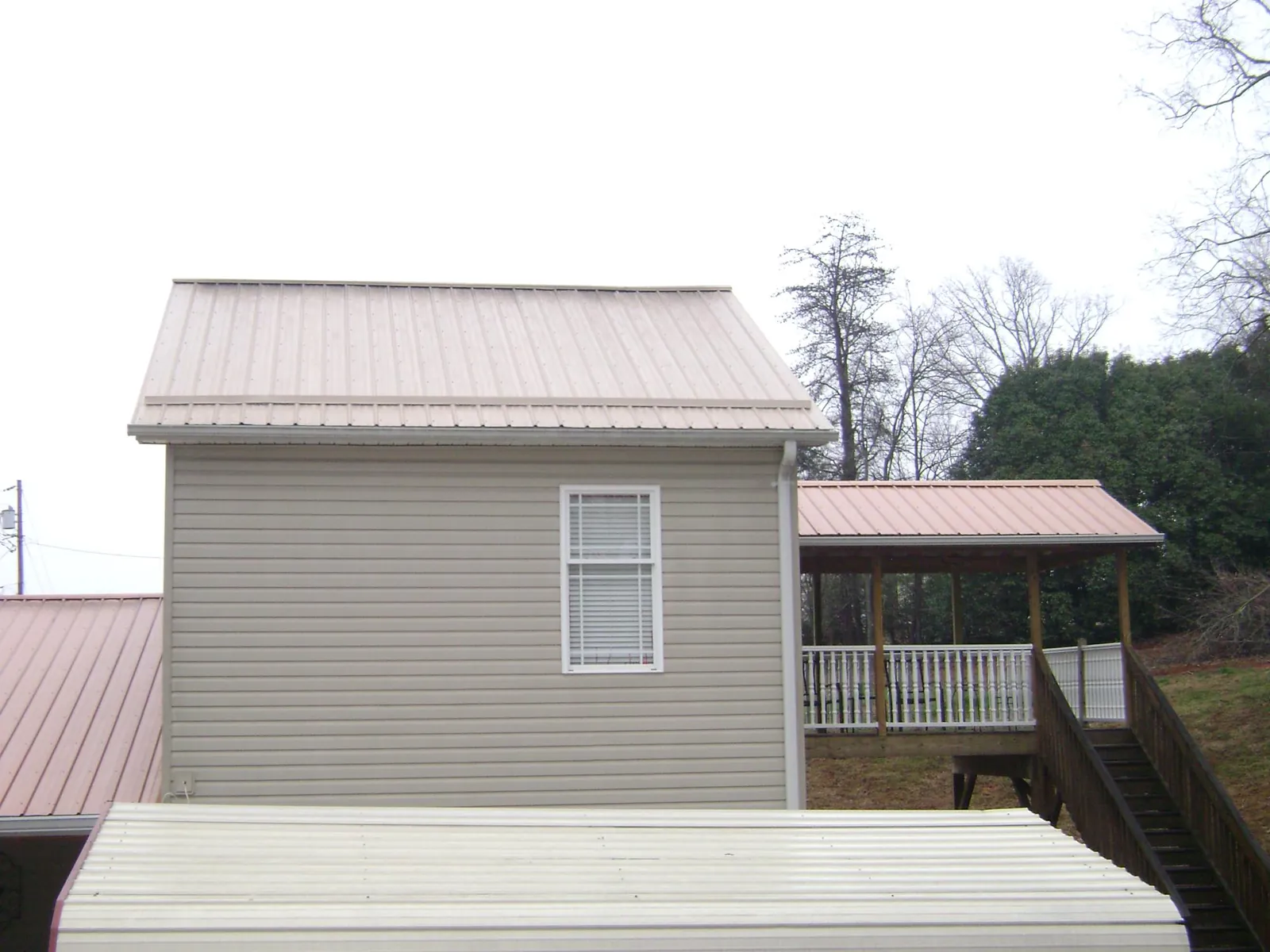 Tan metal roofs on a two story addition and attached porch, from a Roof Replacement job in Tarboro